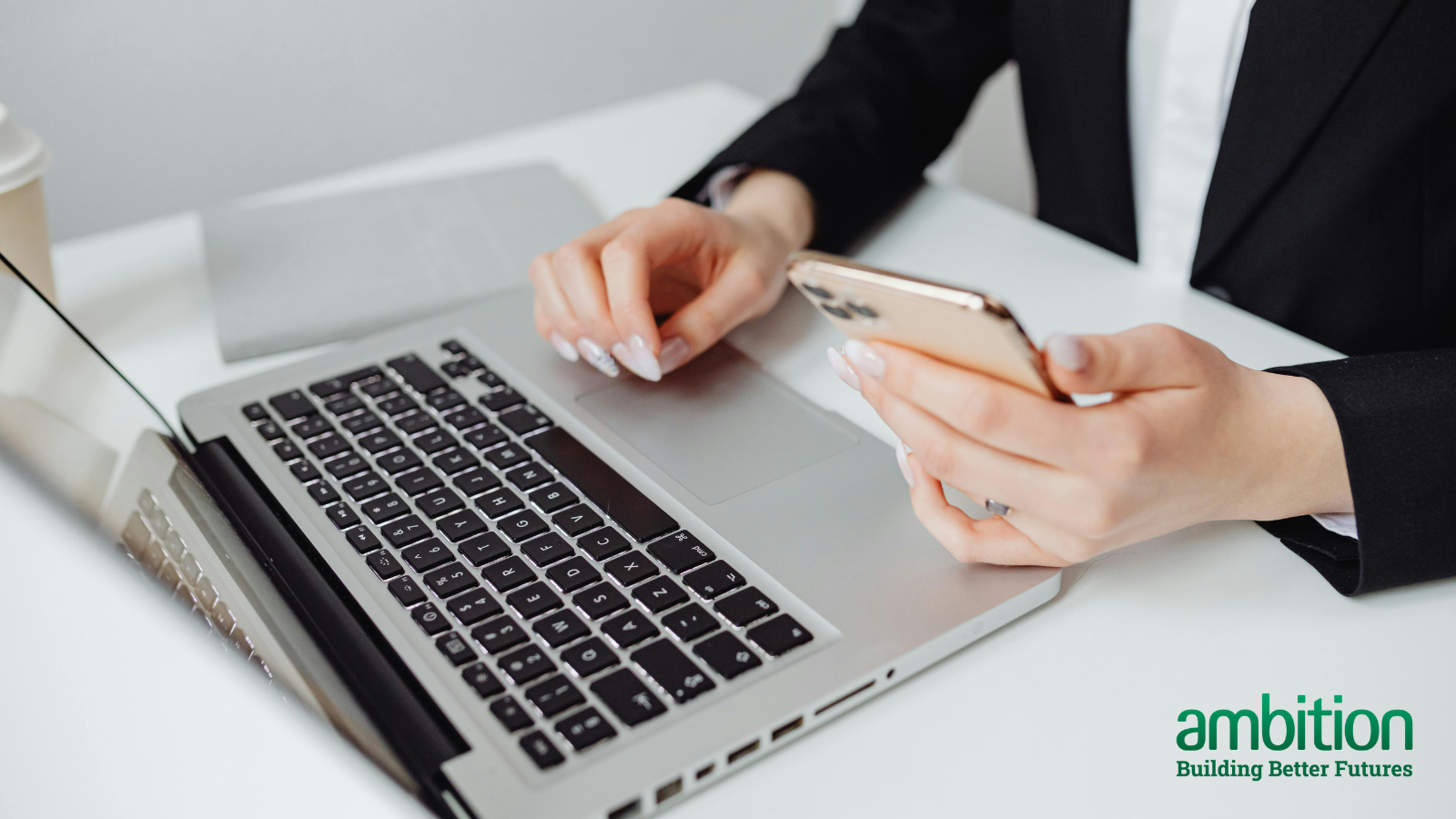 Person sitting at a desk with a laptop in front of them and a phone in their hand