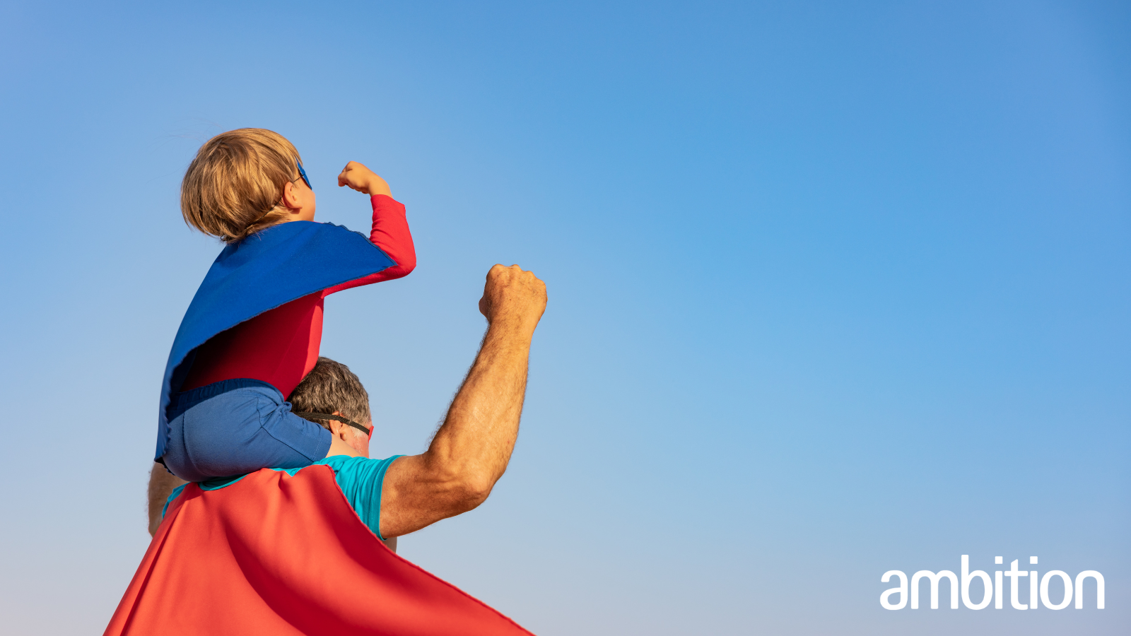 Small boy sitting on the shoulders of his father, both dressed in a superhero cape
